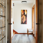 Looking-into-the-hallway-with-glass-blocks-to-the-left-a-doorway-to-the-stairs-and-abstract-flower-artwork-at-the-end