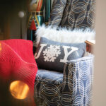 joy-pillow-in-on-patterned-couch-with-red-throw-blanket-across-the-arm