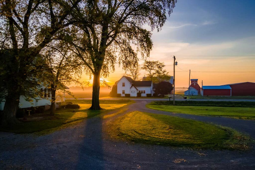 A quaint farmhouse in the background with a glowing sunset illustrates a beautiful farm countryside setting.