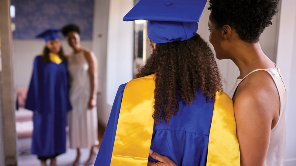 Daughter and mother look at reflection In mirror on graduation day