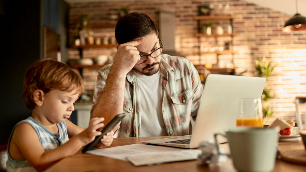 Kid playing on phone while dad looks at finances