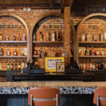 View Of Bar With Brick Wall Featuring Neatly Organized Liquor Bottles