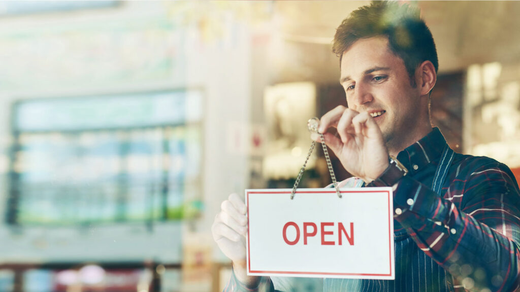 Smiling man holding an OPEN sign at window of small business