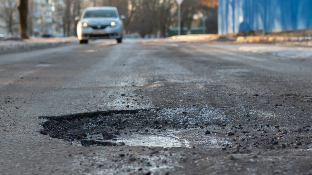 A Car Coming Down The Street About To Hit A Pothole