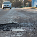 A Car Coming Down The Street About To Hit A Pothole