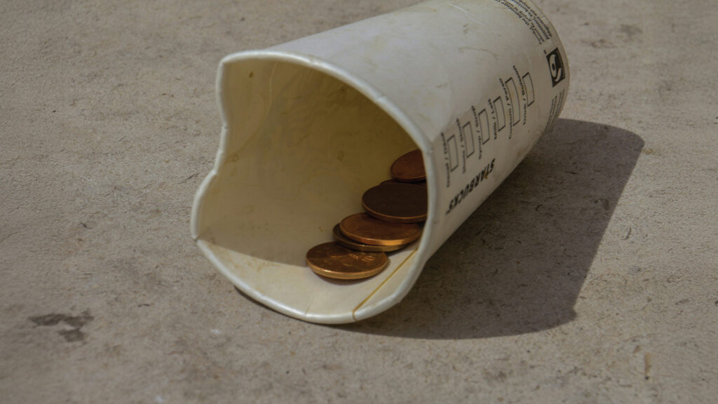 Disposable Cup On The Ground With A Few Coins Inside