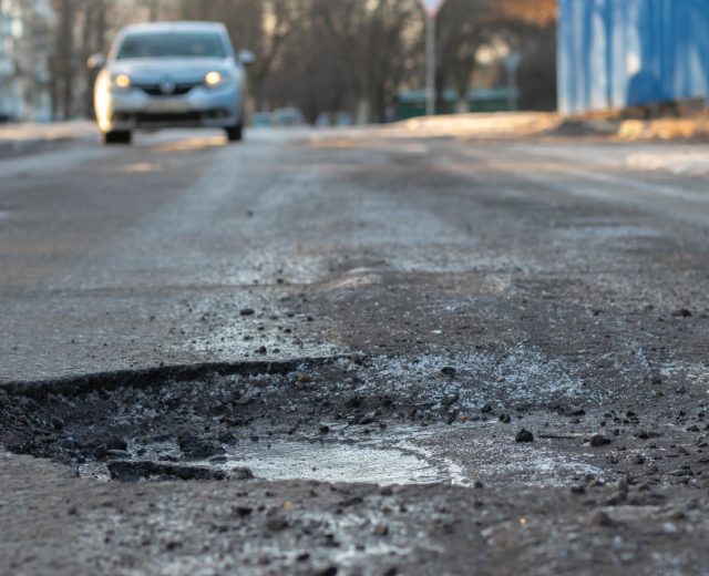 A Car Coming Down The Street About To Hit A Pothole