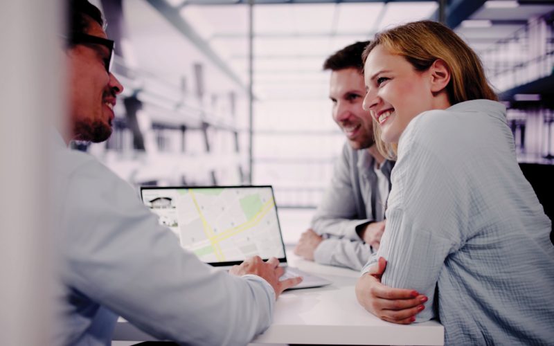 Featured Couple And Realtor Looking At House Listing On Map