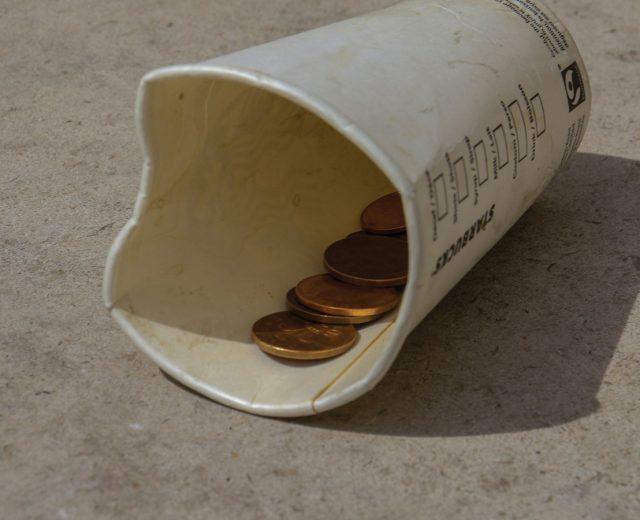 Disposable Cup On The Ground With A Few Coins Inside