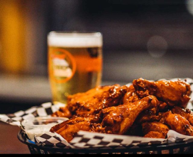 A diner-style plate of fresh, hot chicken wings, with a cold glass of beer in the background.