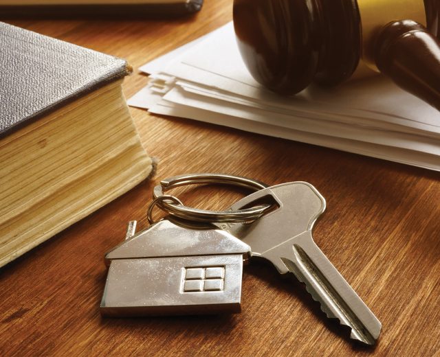 Judges gavel lays on desk next to keychain with a home key