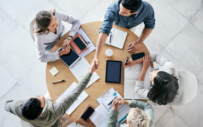 Overhead view of group of people meeting at a table shaking hands Featuredimage