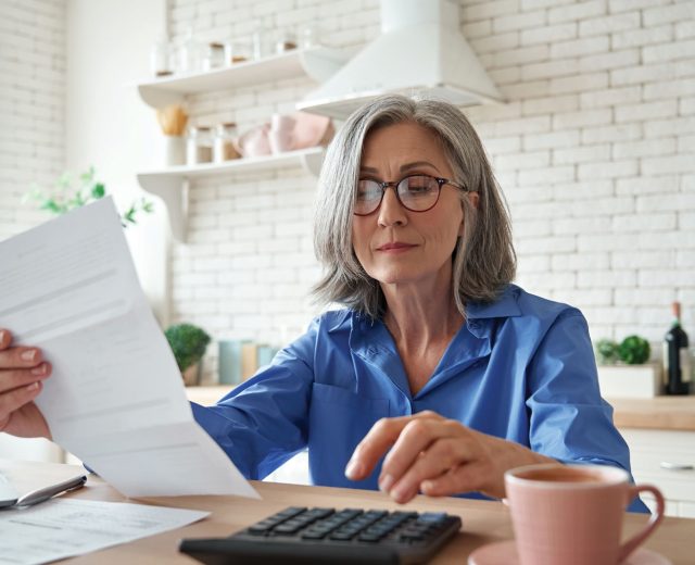 Senior woman calculating money budget tax sitting at kitchen table